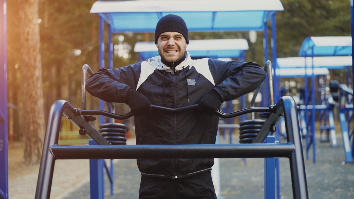 Attractive young man doing exercise in outdoor gym in winter park